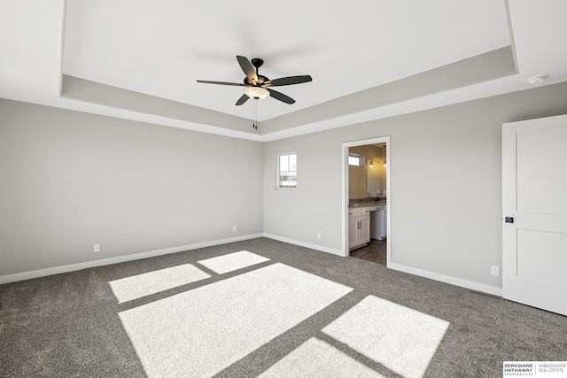 unfurnished bedroom with ceiling fan, a raised ceiling, and ensuite bath