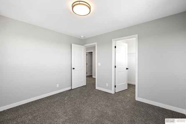 unfurnished bedroom featuring a spacious closet, a closet, and dark carpet