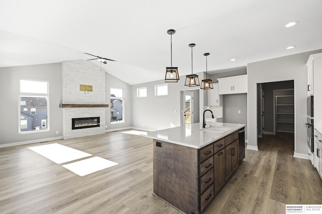 kitchen featuring white cabinetry, sink, hanging light fixtures, a stone fireplace, and dark brown cabinets