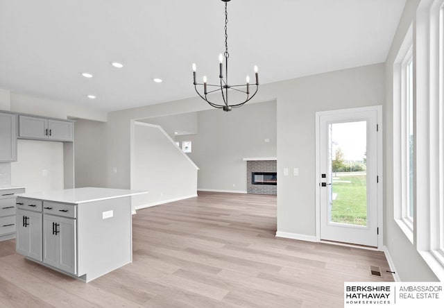 kitchen featuring gray cabinetry, light hardwood / wood-style floors, a kitchen island, a brick fireplace, and decorative light fixtures