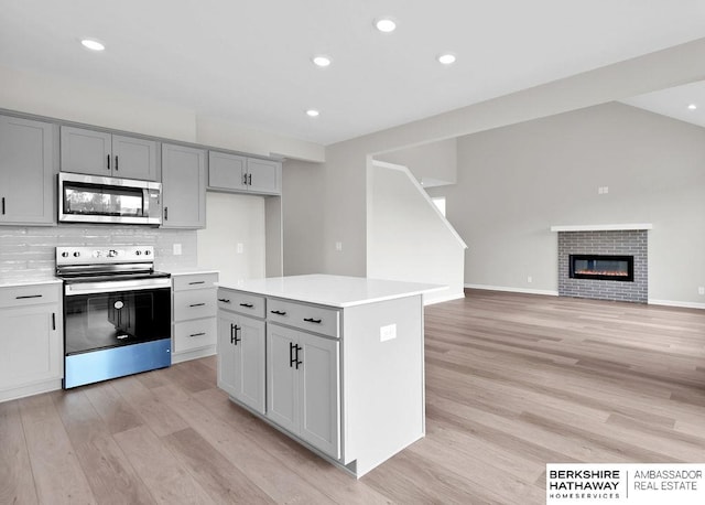 kitchen featuring gray cabinetry, light wood-type flooring, a kitchen island, stainless steel appliances, and decorative backsplash