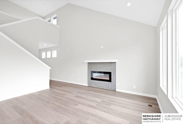 unfurnished living room featuring a brick fireplace, high vaulted ceiling, and light hardwood / wood-style floors