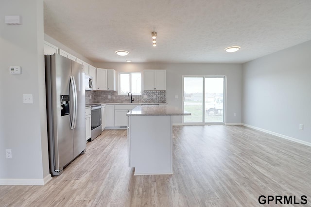 kitchen with sink, appliances with stainless steel finishes, white cabinetry, tasteful backsplash, and a kitchen island