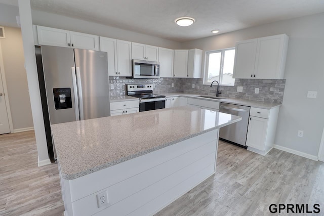 kitchen with appliances with stainless steel finishes, a kitchen island, white cabinetry, sink, and light stone countertops