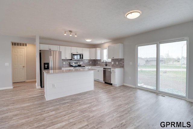 kitchen with sink, appliances with stainless steel finishes, white cabinetry, a center island, and a healthy amount of sunlight