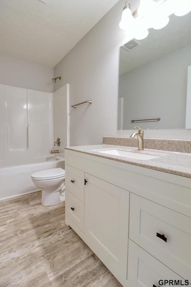 full bathroom featuring shower / tub combination, vanity, wood-type flooring, a textured ceiling, and toilet