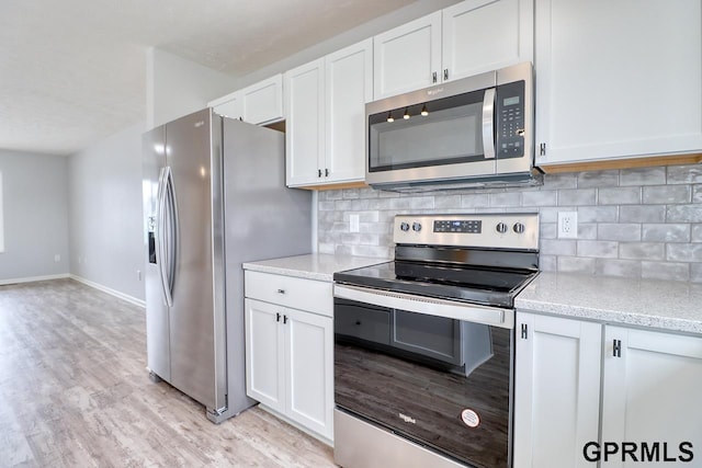 kitchen with appliances with stainless steel finishes, white cabinetry, light stone countertops, light hardwood / wood-style floors, and decorative backsplash