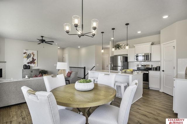 dining space featuring ceiling fan with notable chandelier, a fireplace, sink, and light wood-type flooring