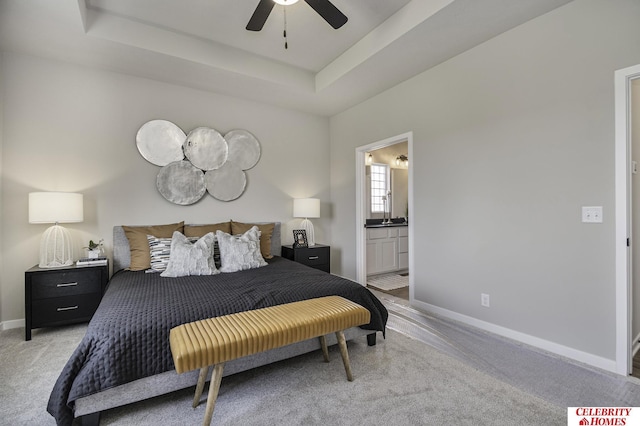 bedroom featuring a tray ceiling, light colored carpet, ceiling fan, and ensuite bathroom