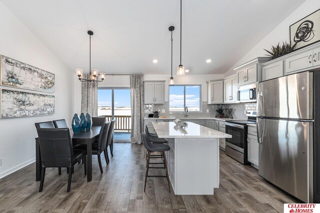 kitchen with stainless steel appliances, decorative light fixtures, vaulted ceiling, and a kitchen island