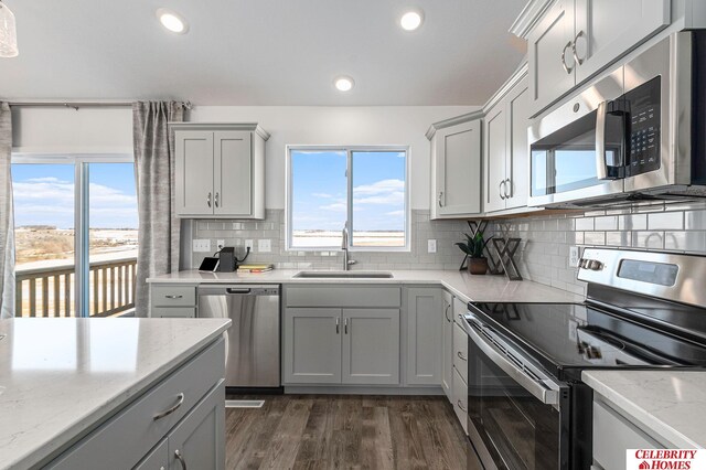 kitchen with sink, light stone counters, appliances with stainless steel finishes, gray cabinets, and decorative backsplash