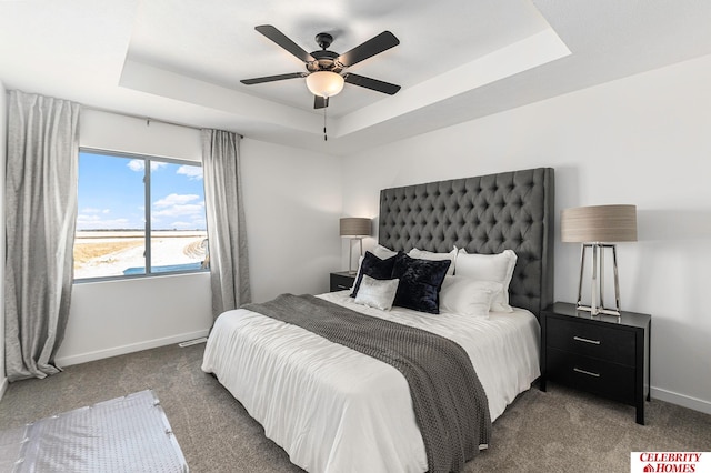 bedroom with ceiling fan, a tray ceiling, and dark carpet