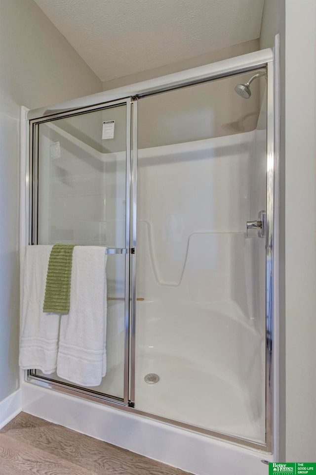 bathroom with a shower with shower door, hardwood / wood-style floors, and a textured ceiling