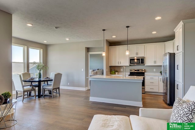 kitchen with appliances with stainless steel finishes, white cabinets, dark hardwood / wood-style floors, a kitchen island with sink, and pendant lighting