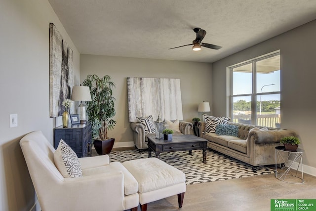 living area featuring baseboards, wood finished floors, ceiling fan, and a textured ceiling