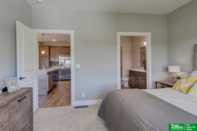 bedroom featuring stainless steel refrigerator with ice dispenser, light carpet, and connected bathroom