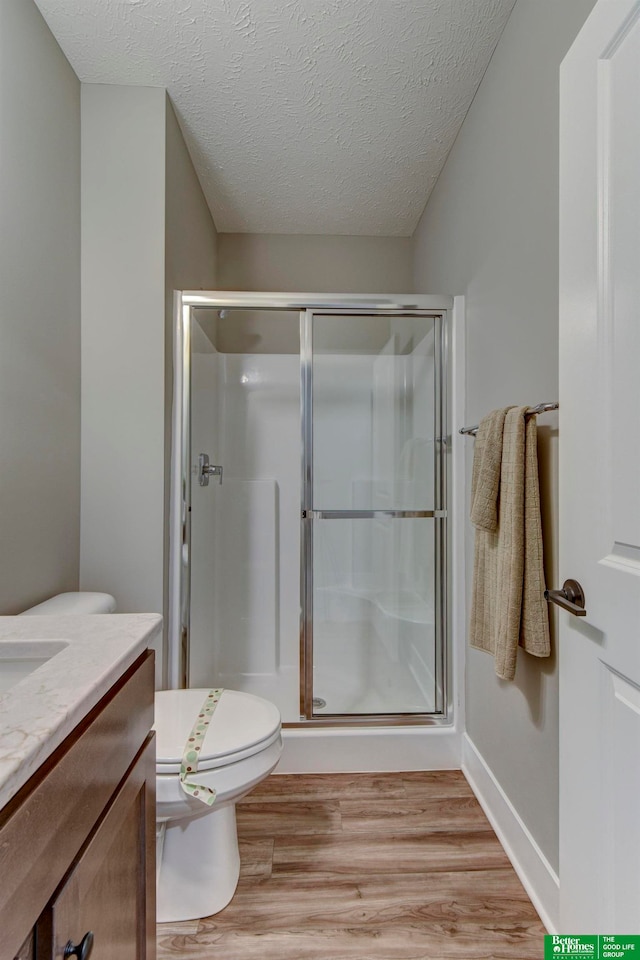 bathroom with a textured ceiling, hardwood / wood-style floors, a shower with door, vanity, and toilet