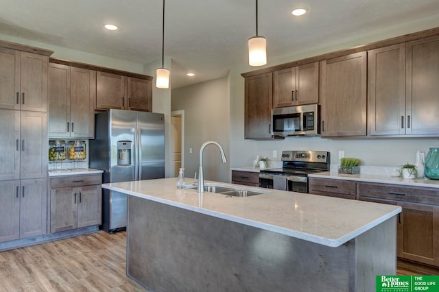 kitchen with stainless steel appliances, a center island with sink, sink, and light wood-type flooring