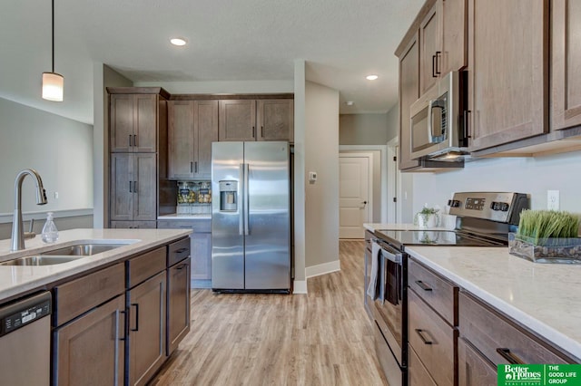 kitchen featuring light hardwood / wood-style floors, light stone countertops, hanging light fixtures, appliances with stainless steel finishes, and sink