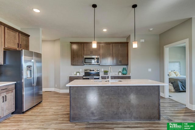 kitchen with appliances with stainless steel finishes, light hardwood / wood-style floors, and a center island with sink