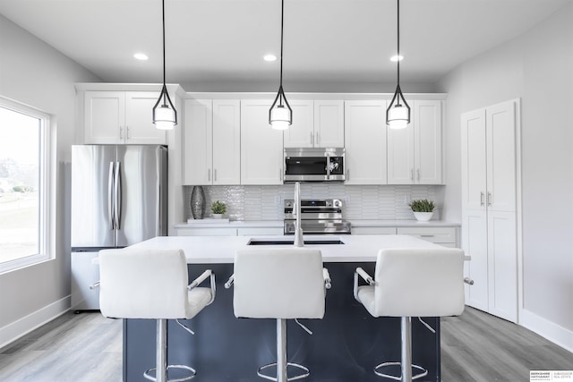 kitchen with pendant lighting, a center island with sink, a breakfast bar, white cabinetry, and stainless steel appliances