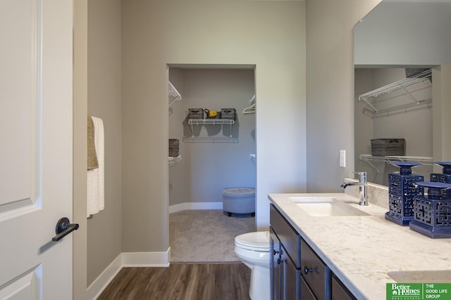 full bath featuring vanity, toilet, wood finished floors, a walk in closet, and baseboards
