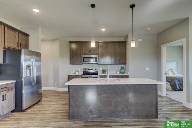 kitchen with decorative light fixtures, a sink, light countertops, appliances with stainless steel finishes, and light wood finished floors