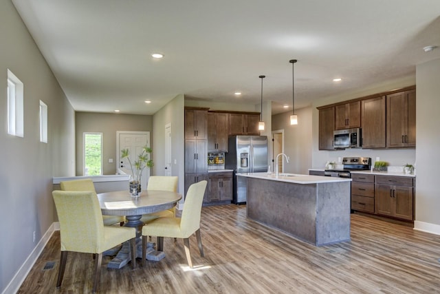 kitchen with recessed lighting, appliances with stainless steel finishes, wood finished floors, a sink, and a center island with sink