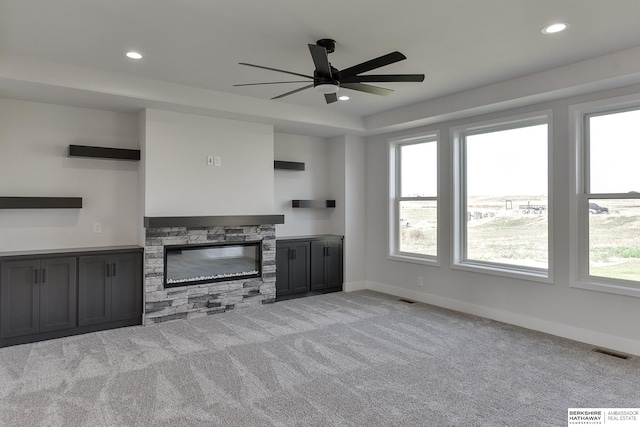 unfurnished living room with a wealth of natural light, a stone fireplace, and light colored carpet