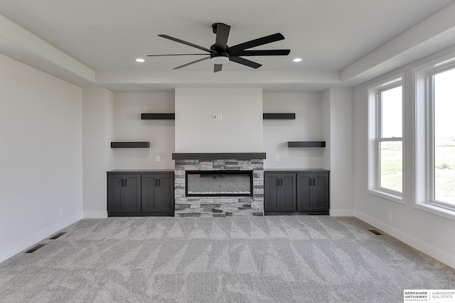 unfurnished living room featuring a healthy amount of sunlight, ceiling fan, a stone fireplace, and light colored carpet