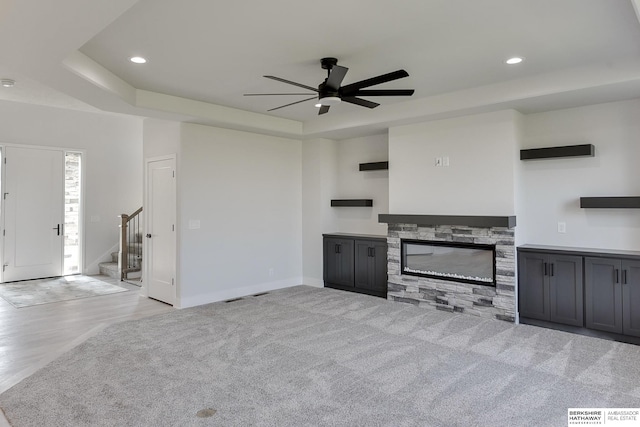 unfurnished living room featuring ceiling fan, a fireplace, light wood-type flooring, and a raised ceiling