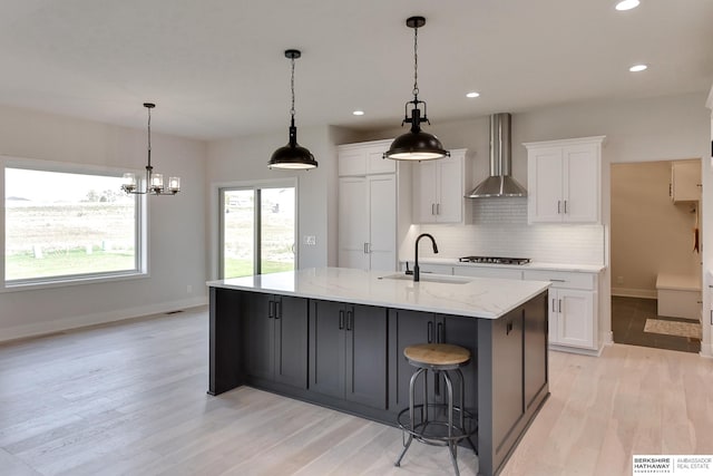 kitchen featuring wall chimney range hood, light hardwood / wood-style floors, a large island with sink, sink, and white cabinets