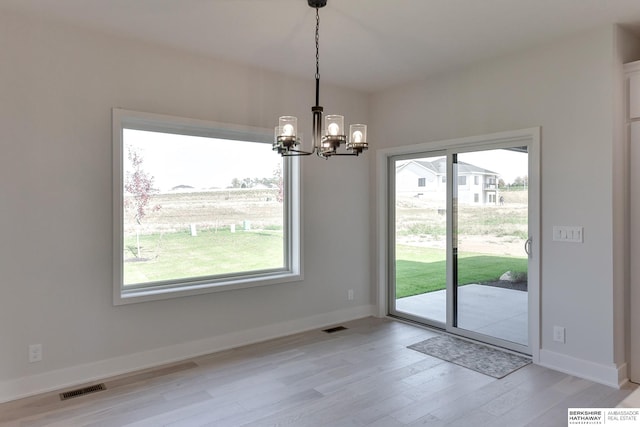 unfurnished dining area with light wood-type flooring, a chandelier, and a healthy amount of sunlight