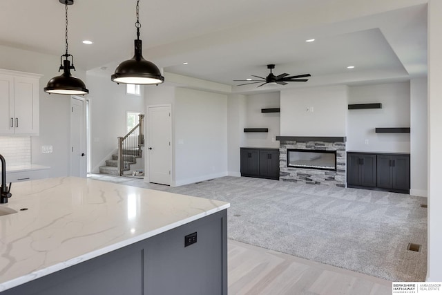 kitchen with pendant lighting, light carpet, a stone fireplace, light stone countertops, and white cabinets