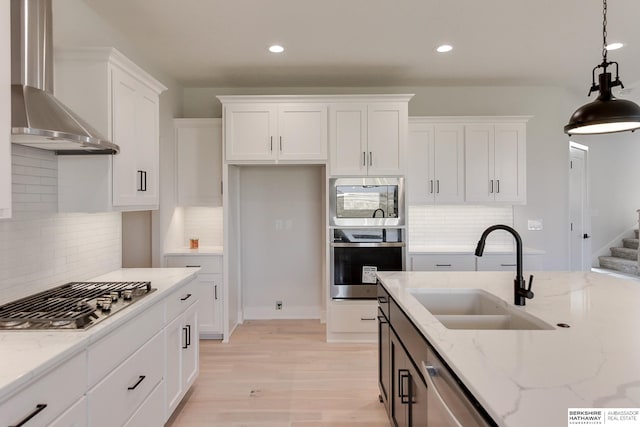 kitchen with wall chimney exhaust hood, pendant lighting, sink, white cabinets, and appliances with stainless steel finishes