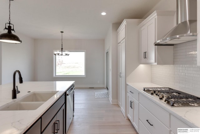 kitchen with stainless steel appliances, white cabinets, wall chimney exhaust hood, sink, and hanging light fixtures