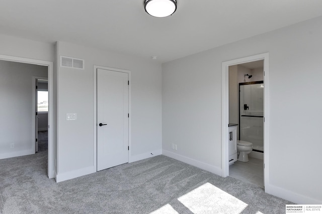 unfurnished bedroom with a closet, light colored carpet, and ensuite bath