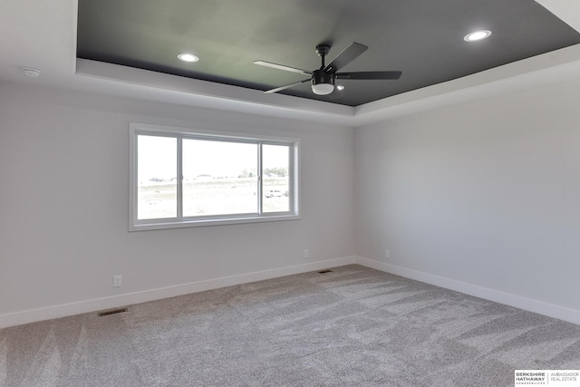 carpeted spare room featuring ceiling fan and a tray ceiling