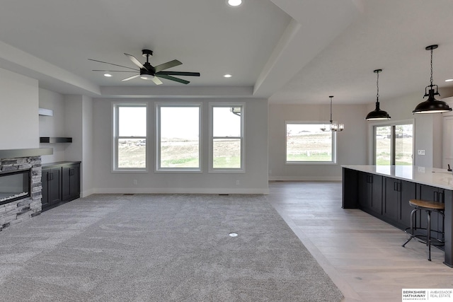 unfurnished living room with a stone fireplace, ceiling fan with notable chandelier, light hardwood / wood-style flooring, and plenty of natural light