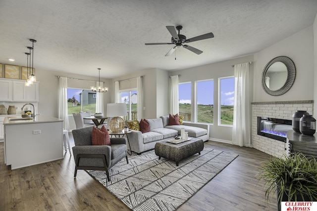 living room with a textured ceiling, hardwood / wood-style flooring, ceiling fan with notable chandelier, and a brick fireplace