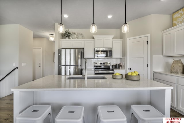 kitchen featuring pendant lighting, white cabinetry, stainless steel appliances, and an island with sink