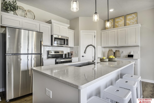 kitchen featuring pendant lighting, a kitchen island with sink, sink, white cabinetry, and stainless steel appliances