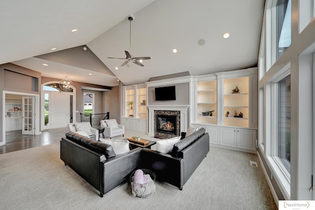 living room with a premium fireplace, built in features, high vaulted ceiling, and ceiling fan with notable chandelier