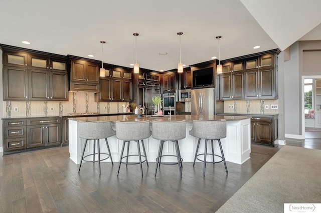 kitchen with hanging light fixtures, dark hardwood / wood-style floors, appliances with stainless steel finishes, a large island, and dark brown cabinetry