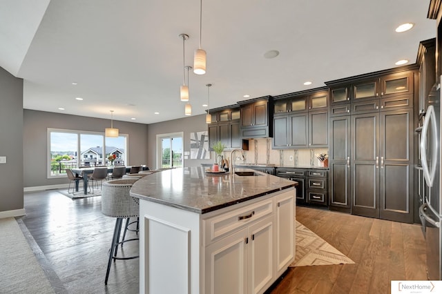 kitchen with dark brown cabinets, a kitchen island with sink, sink, decorative light fixtures, and white cabinets