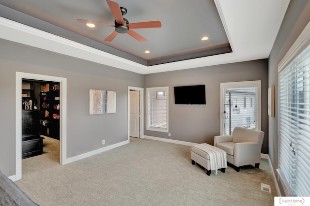 sitting room featuring light carpet, a tray ceiling, and ceiling fan