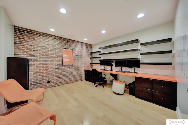 office space with built in desk, light hardwood / wood-style flooring, and brick wall