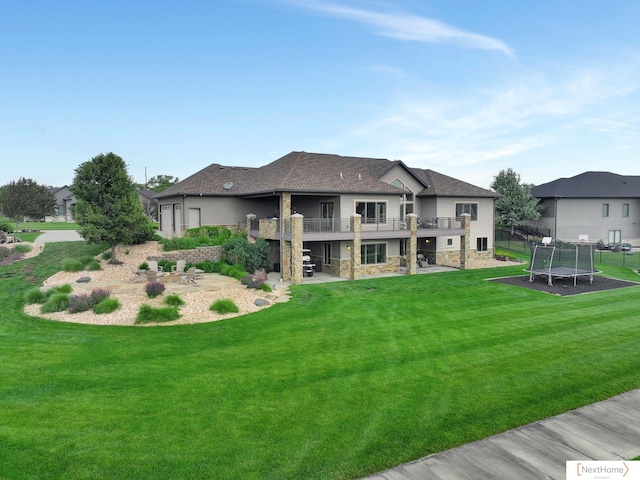 rear view of property featuring a trampoline, a balcony, and a yard