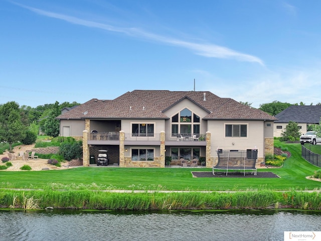 back of house with a lawn, a balcony, a water view, and a trampoline