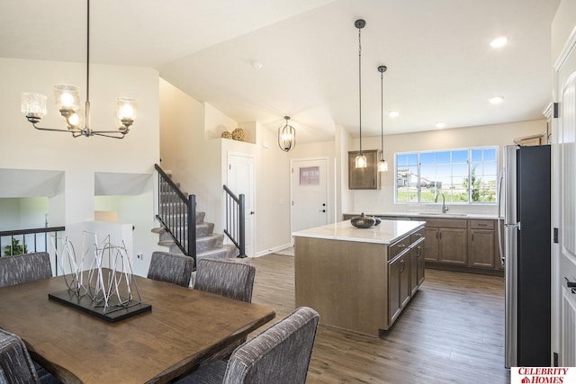 kitchen with sink, vaulted ceiling, decorative light fixtures, a kitchen island, and stainless steel refrigerator